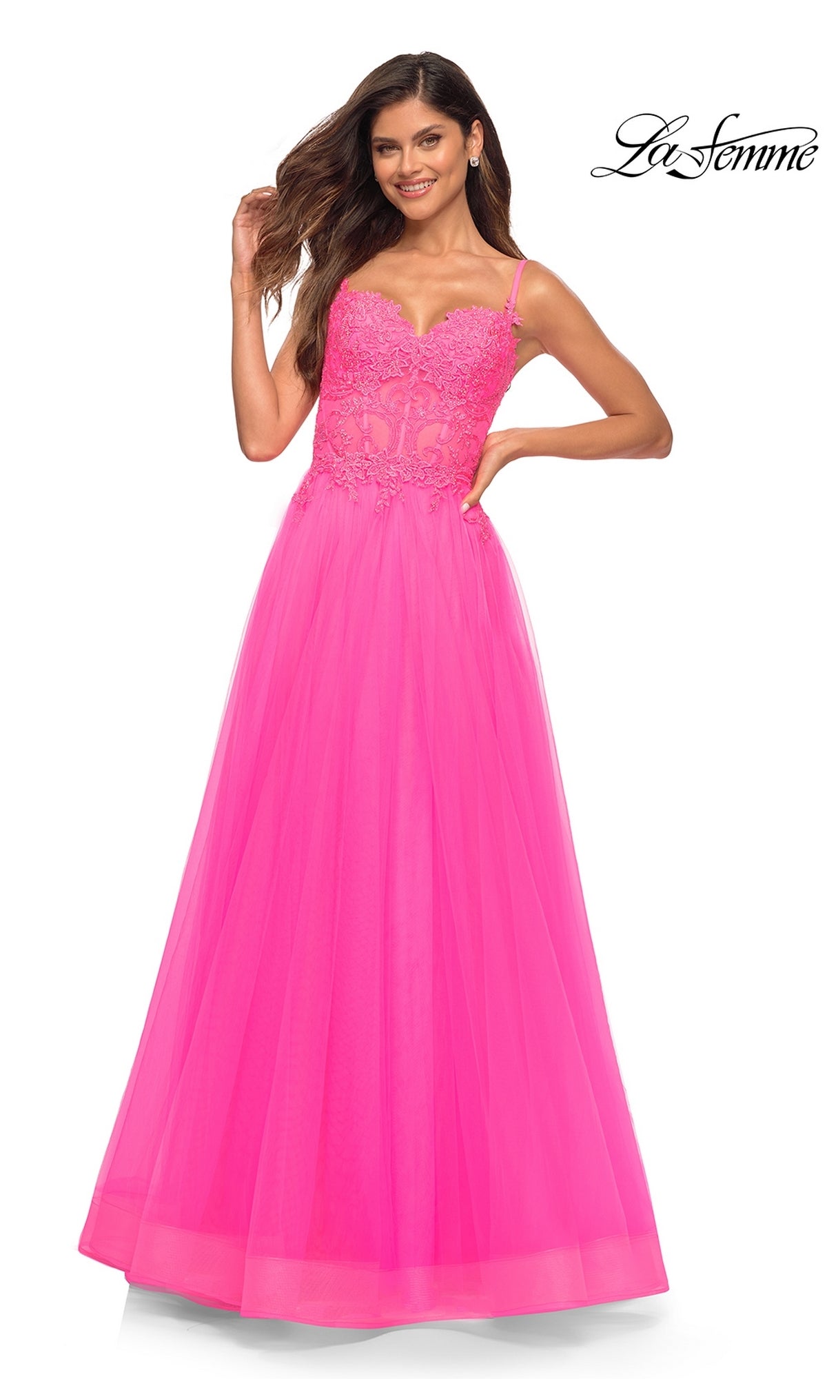 A woman poses against a white background in a La Femme Neon Pink Long Ball Gown with Lace, featuring a fitted bodice and flowing skirt.